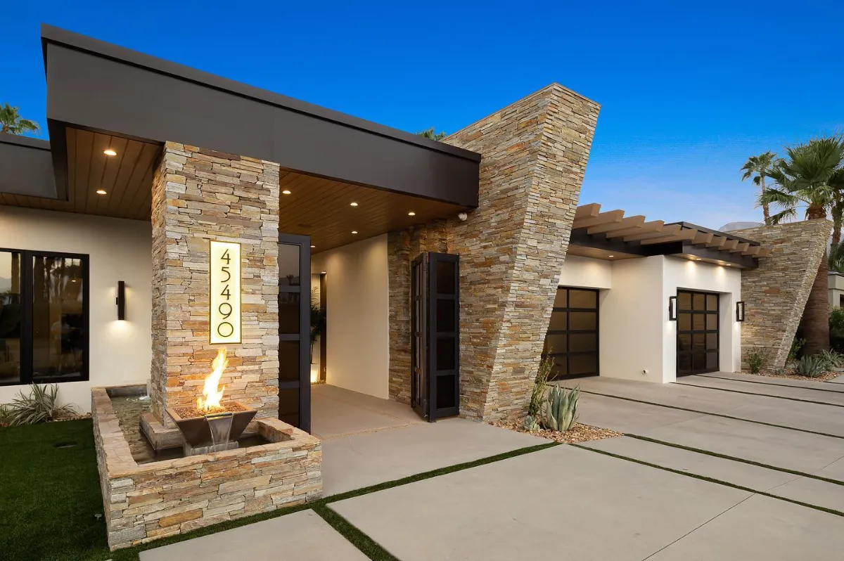 Covered entry court with a lit stacked stone column, address panel and a stone water and fire feature
