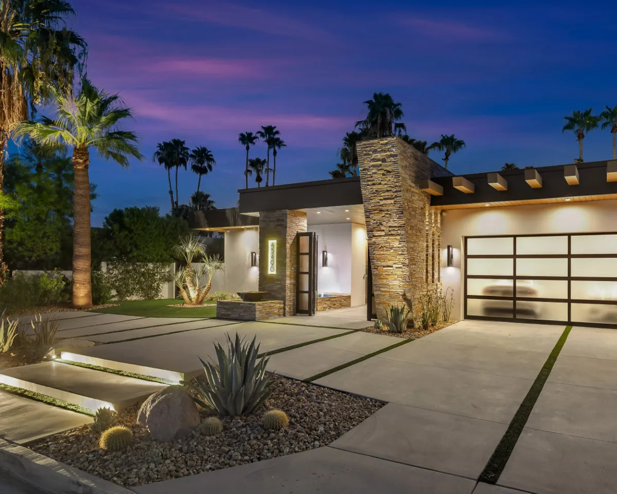 Illuminated entry and glass garage door of a desert modern home under a purple dusk sky