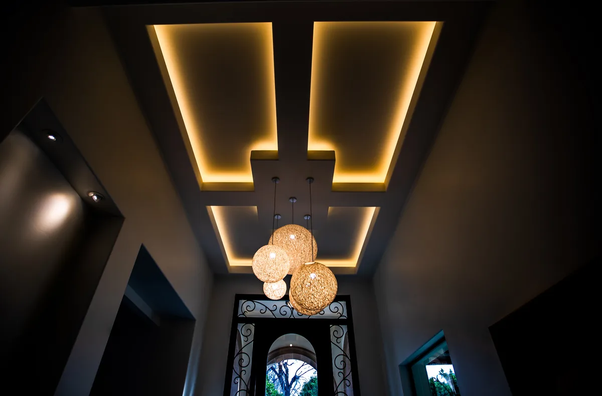 Coffered ceiling with recessed cove lighting above a cluster of woven globe pendants