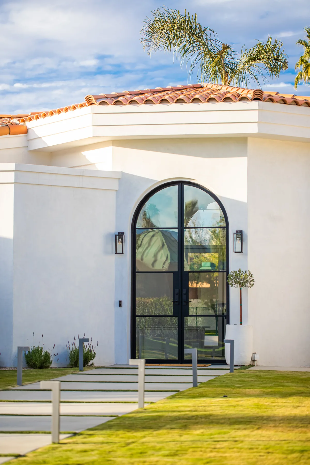 Arched wrought-iron and glass entry door set into a white stucco facade under a tile roof