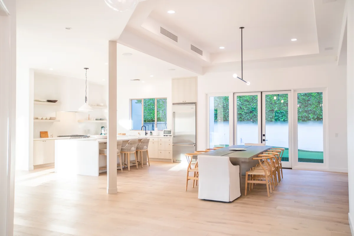 Open kitchen and dining room with a white island, pendant lighting and glass doors to the terrace