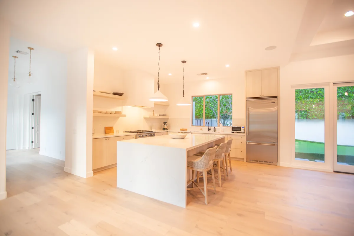 White kitchen with a marble waterfall island, bar seating and stainless appliances