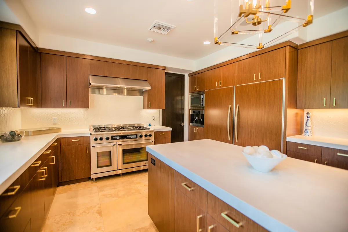 Kitchen with warm timber cabinetry, a professional range and a stone island under a brass fixture