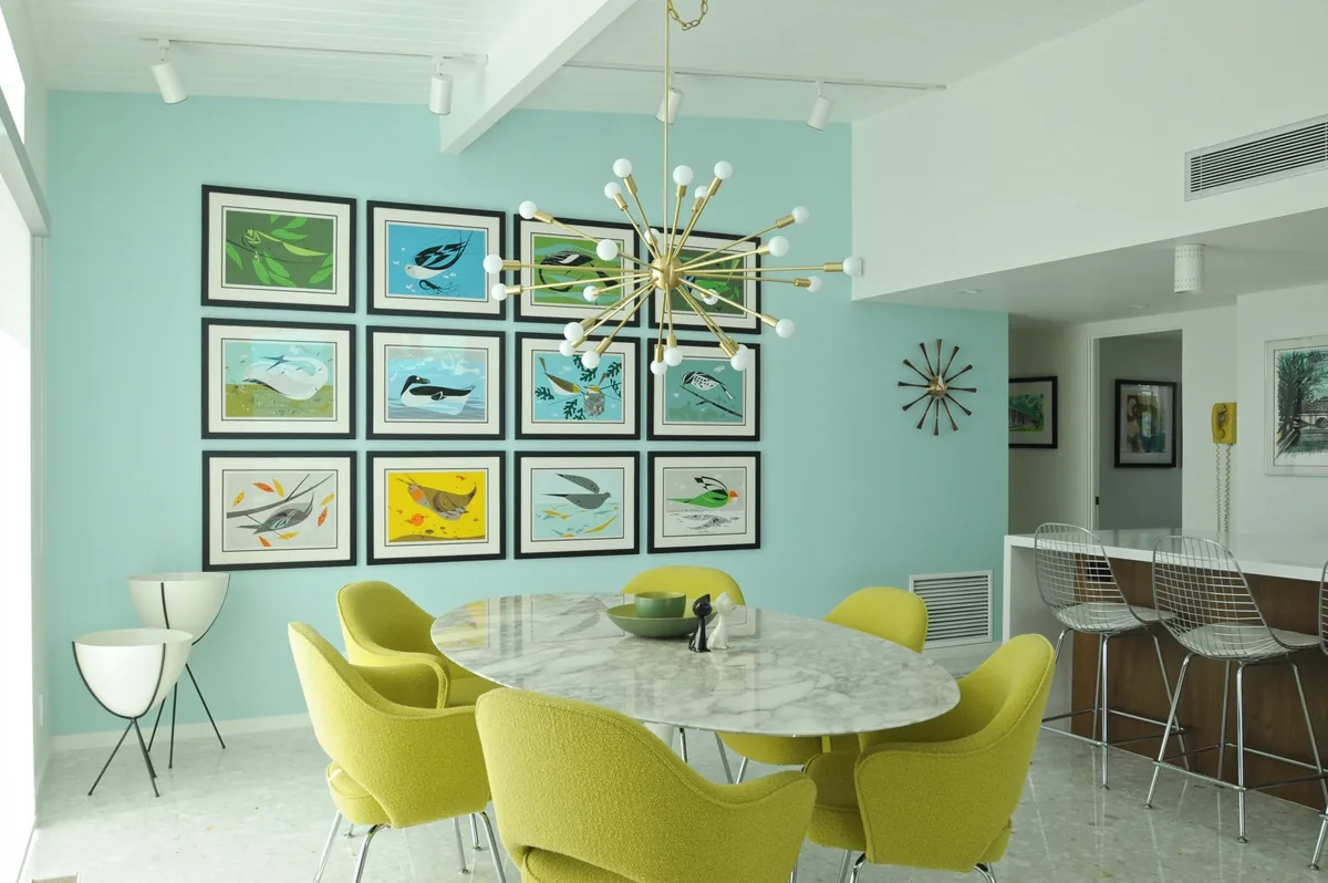 Mid-century dining room with pale green walls, a gallery wall of prints and yellow moulded chairs