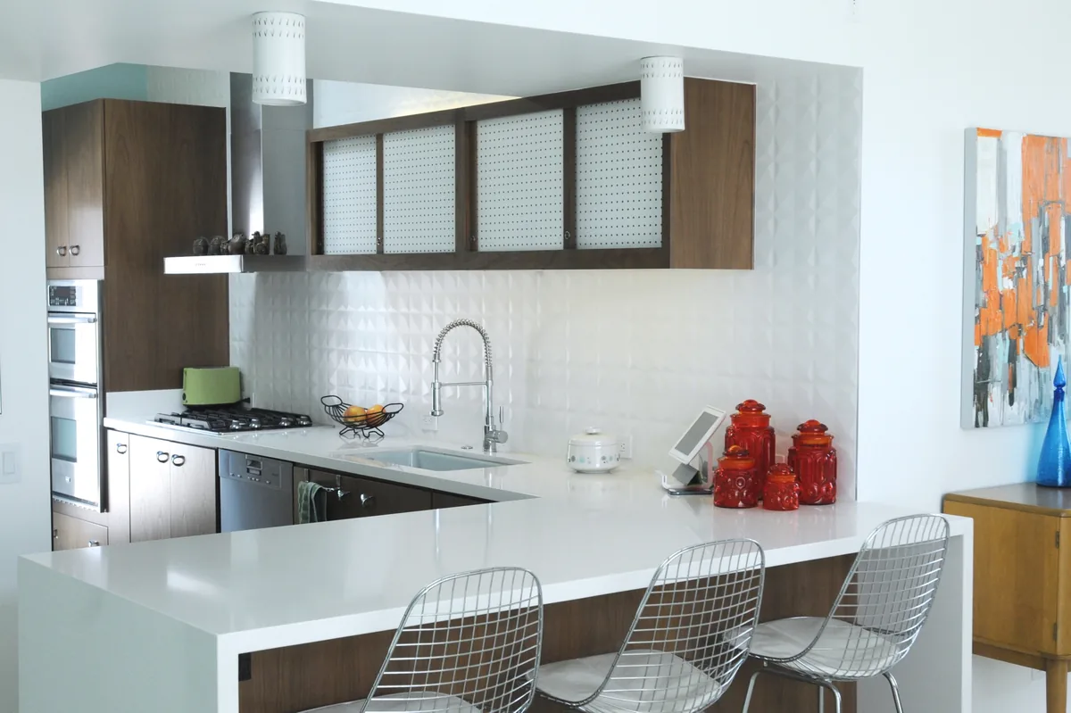 Compact kitchen with white tile, timber shelving and a peninsula with wire bar stools