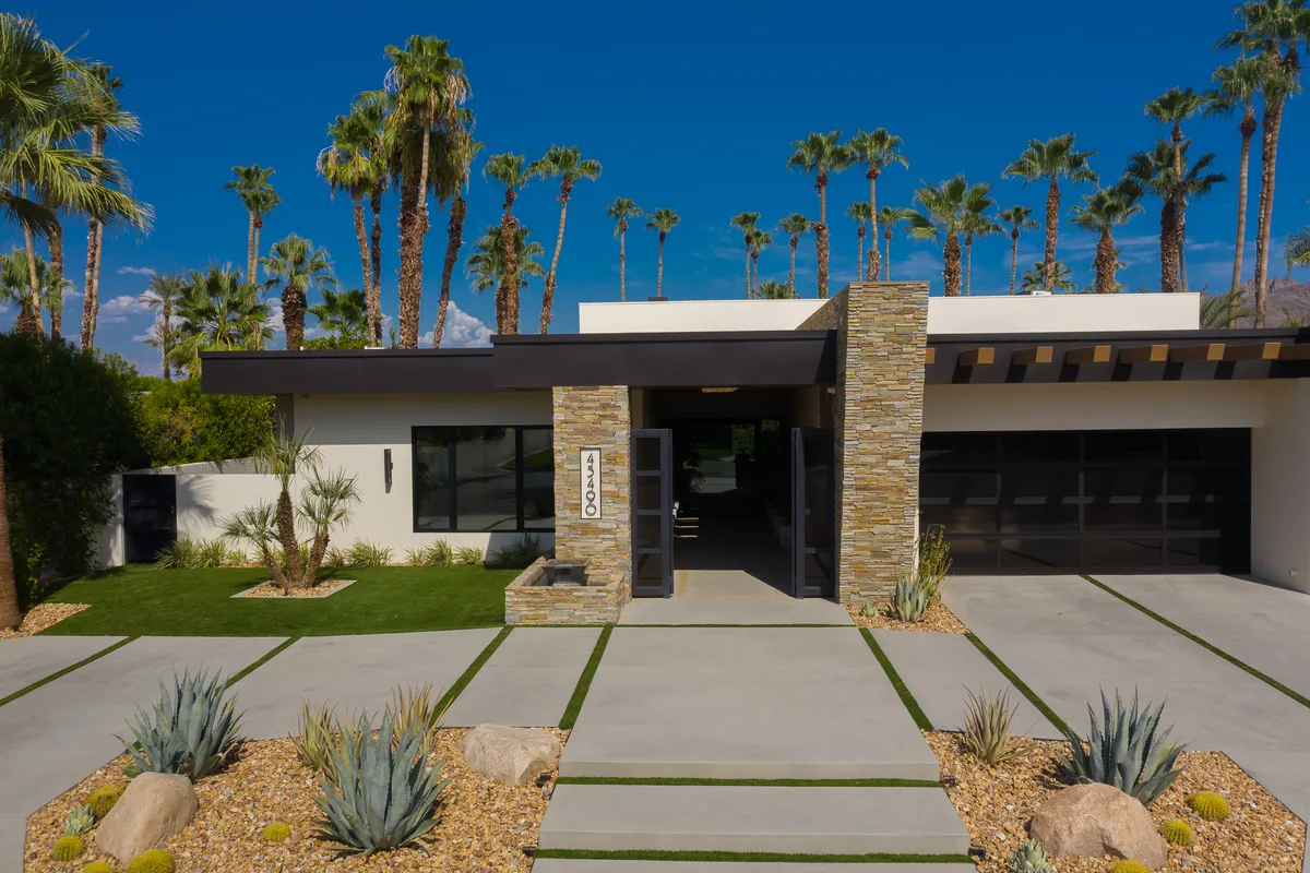 Front elevation in daylight with a banded concrete drive, desert planting and a low-slung roofline