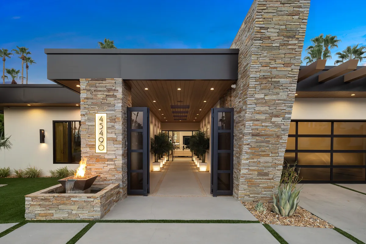 Lit entry courtyard at dusk with a stone-clad column, fire bowl and a recessed front door