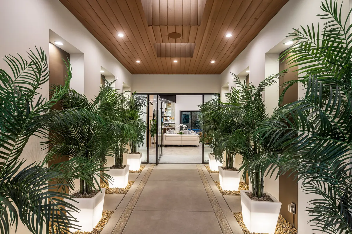 Interior entry hall lined with potted palms under a warm wood ceiling, looking through to the great room