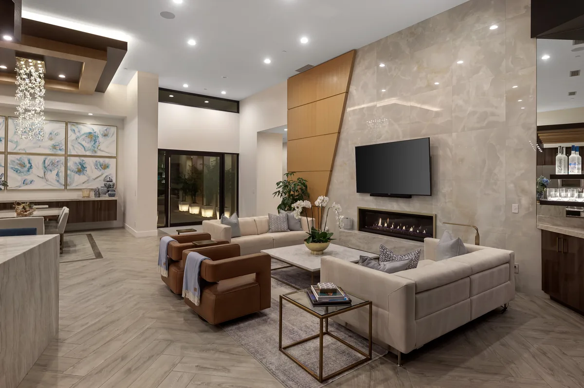 Great room at dusk with a stone fireplace wall, leather seating and glass doors open to the lit pool