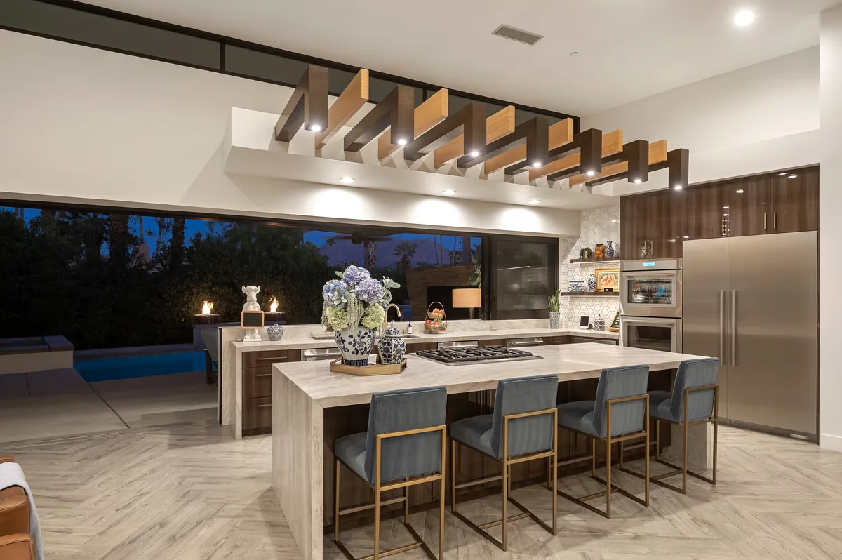 Kitchen with a waterfall stone island, bar seating and exposed timber beams over a wide opening