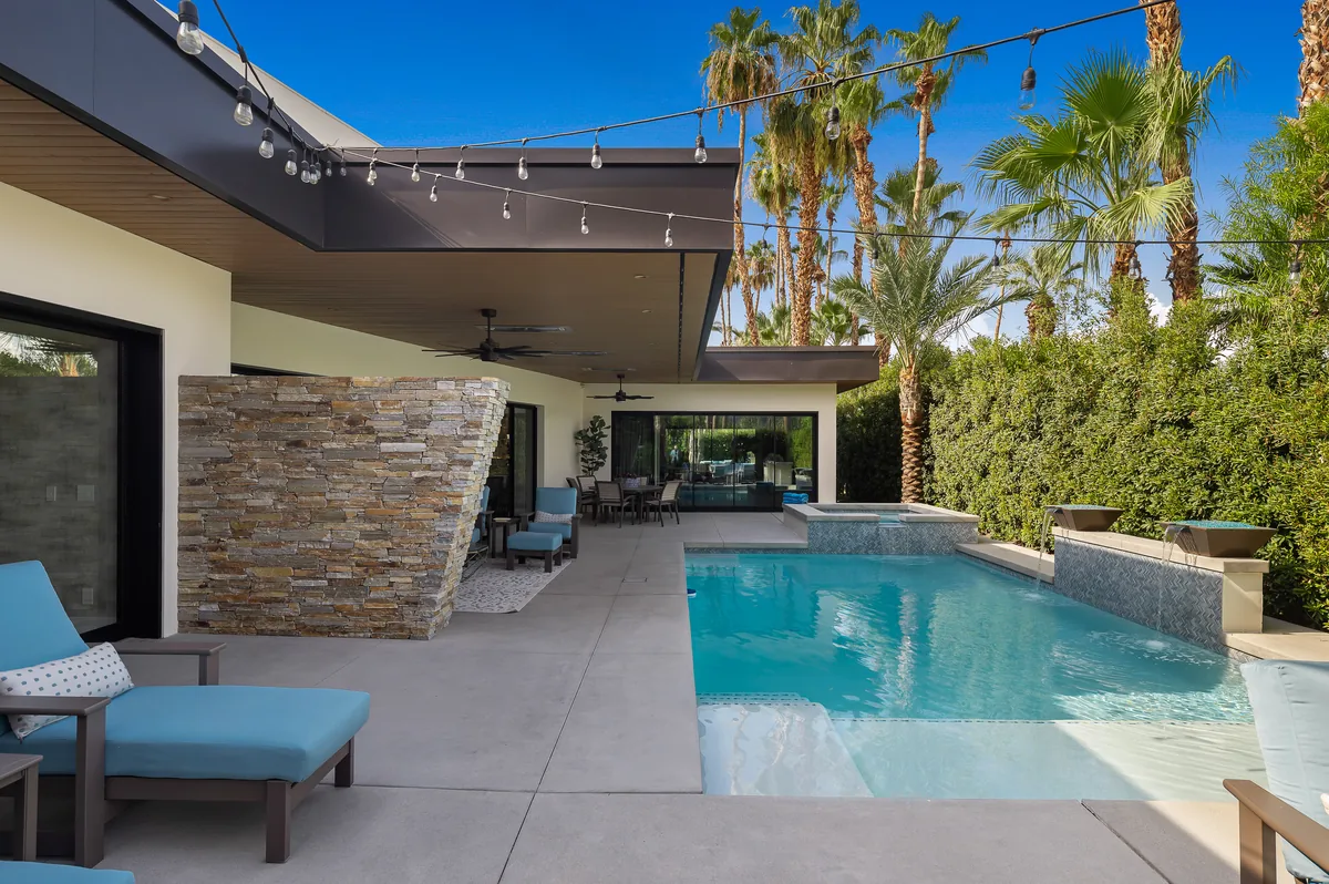 Rectangular pool and raised spa beside a covered patio with a stone column and lounge seating
