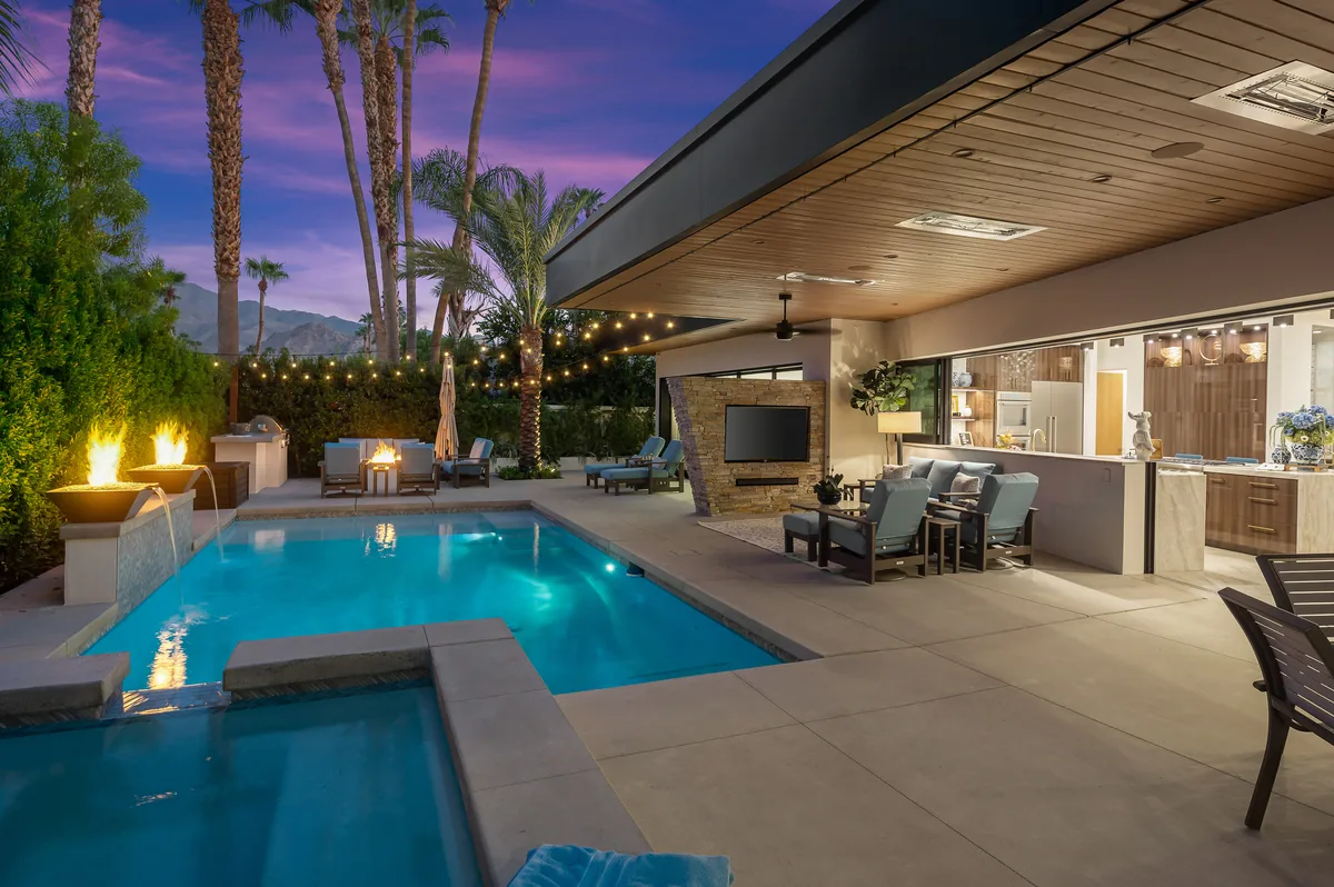 Pool and spa at dusk beneath a covered patio, with lit fire bowls and string lights over a purple desert sky