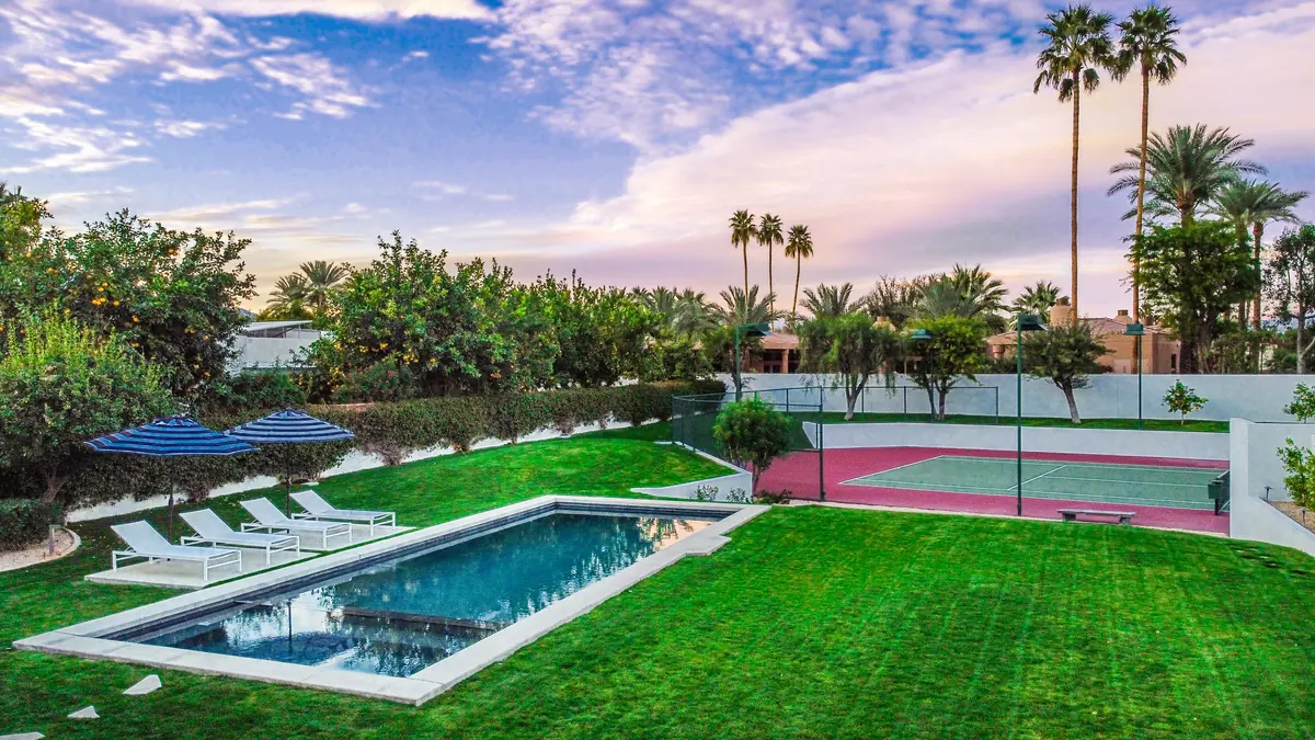 Aerial view at dusk of a rectangular pool, lawn and covered patio framed by tall palms