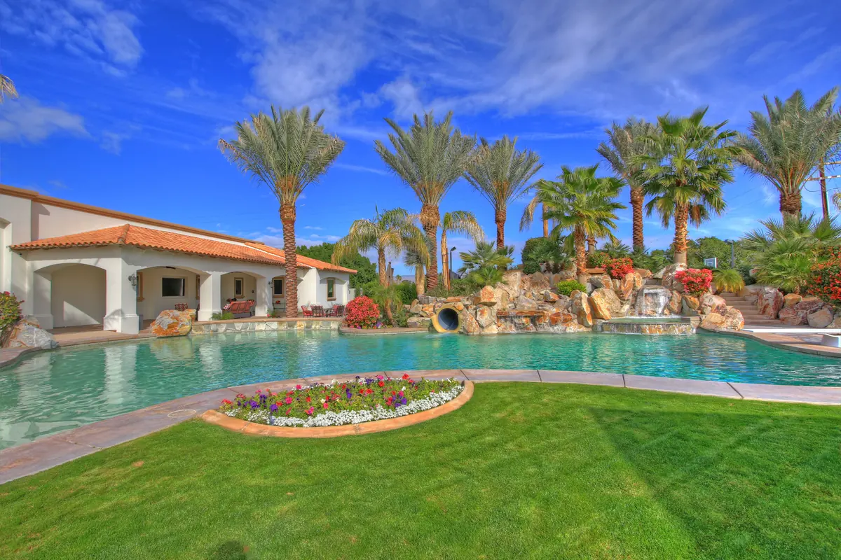 Free-form pool and spa ringed by mature palms, with a raised rock water feature and lawn