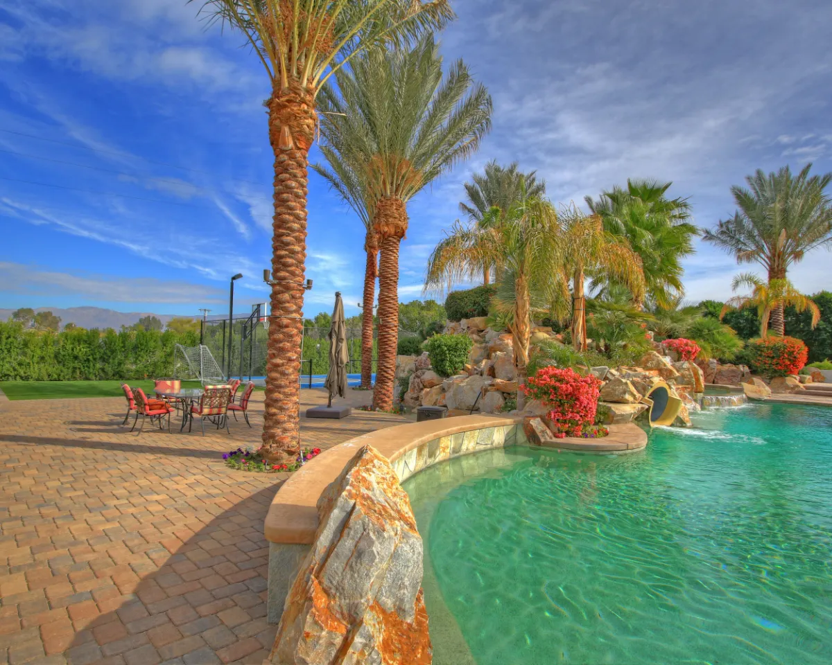 Free-form pool with a stone waterfall, yellow slide, paver patio and mature palms