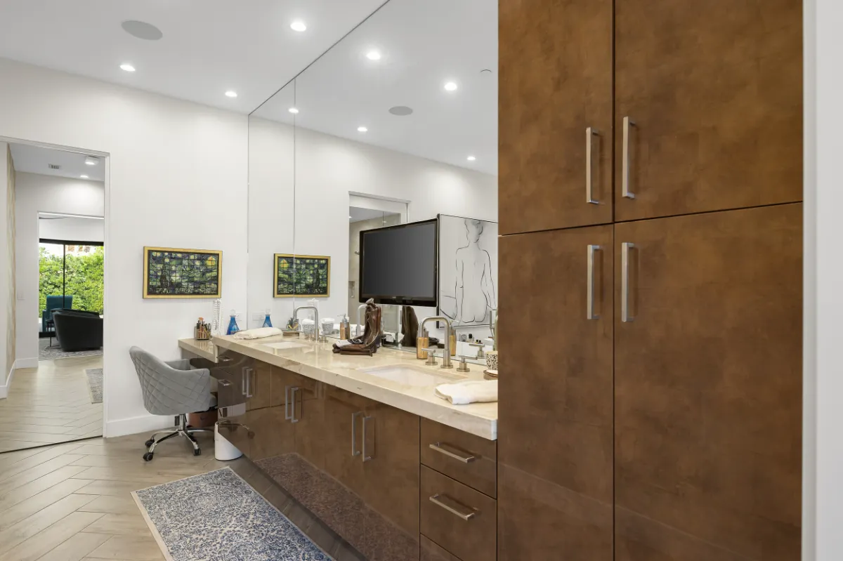 Long walnut double vanity with a stone countertop, full-height mirror and a built-in makeup desk