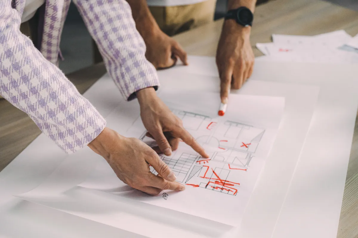 Two people marking up an architectural floor plan in red pen across a table