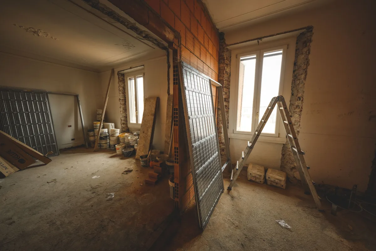A room stripped back to bare walls during a whole house remodel, with a steel lintel over a newly opened doorway and a ladder against the wall