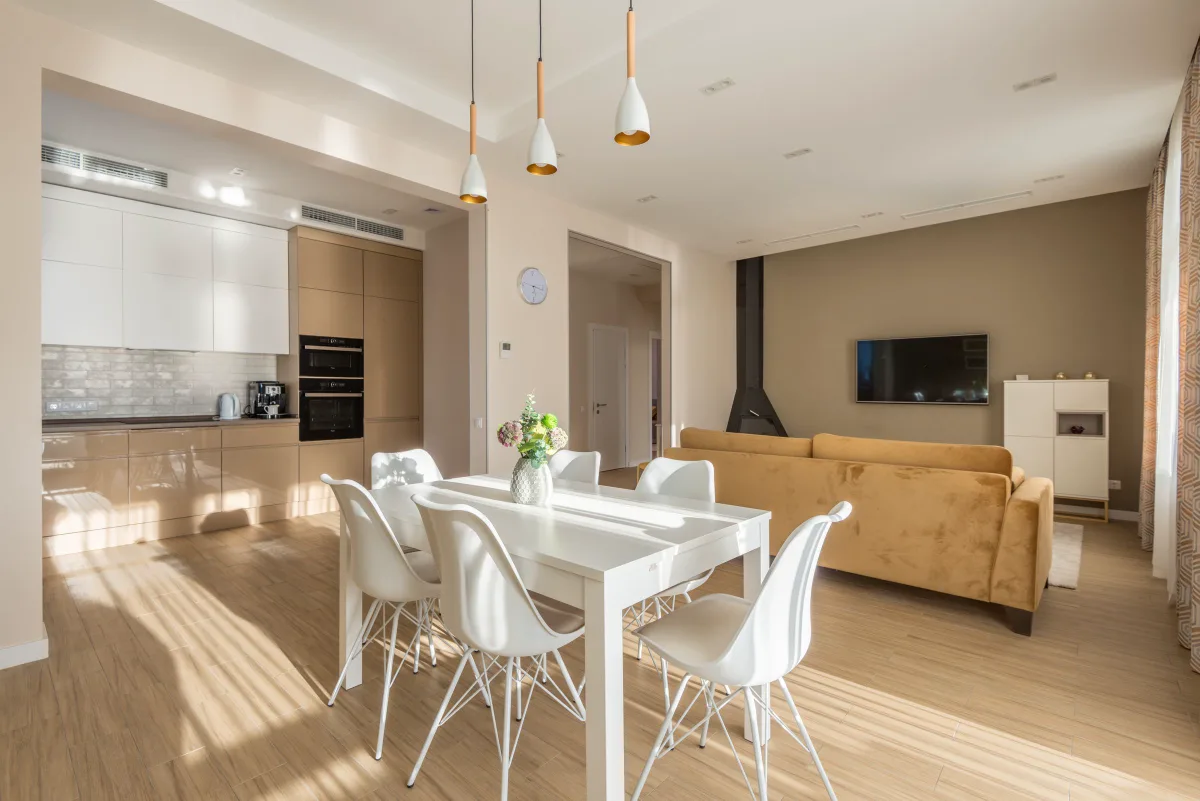 Open kitchen and living space in warm neutrals, with wood cabinetry, wood flooring and off-white walls