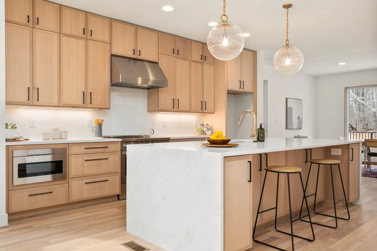 Bright kitchen with pale oak cabinetry, a stone island and pendant lights over it